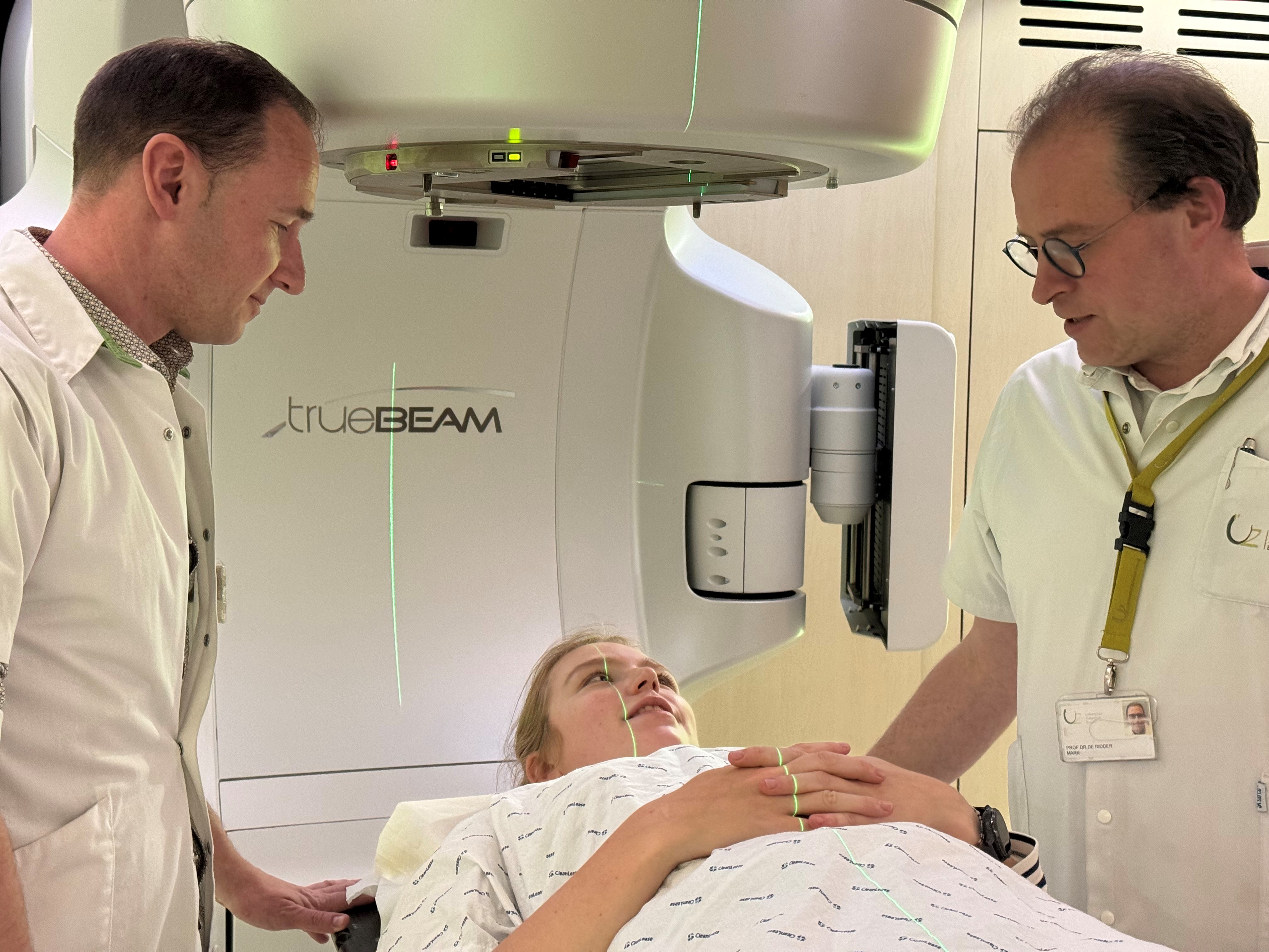 Twee personen in witte kleding staan naast een TrueBeam-medische machine in een klinische ruimte.