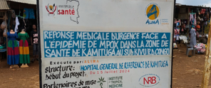 Bord met informatie over de medische respons op de mpox-epidemie in de gezondheidszone van Kamituga, inclusief contactinformatie voor hulpdiensten.