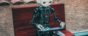 Een robot met een mensachtig gezicht zit op een houten bank en kijkt naar een tablet die hij vasthoudt.