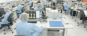 Scientists in blue overalls are working at laboratory tables with computers and microscopes in a clean environment.