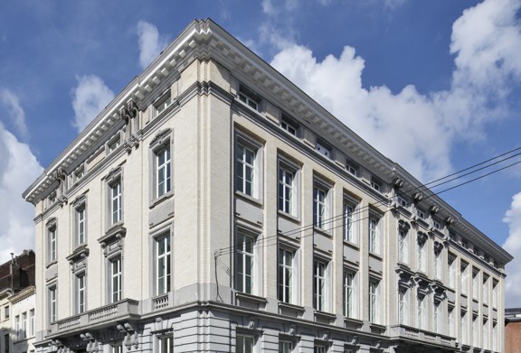 Historisch gebouw met een lichte gevel en opvallende ramen, tegen een blauwe lucht met wolken.