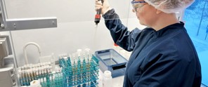 Laboratoriummedewerker gebruikt een pipet boven een rek met buisjes in een schone omgeving.