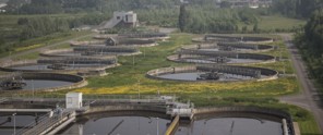Luchtfoto van een rioolwaterzuiveringsinstallatie met meerdere ronde vijvers en groene grasvelden eromheen.