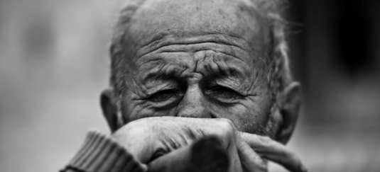 A man in a gray sweater gazes thoughtfully at a blurred background.