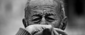 A man in a gray sweater gazes thoughtfully at a blurred background.
